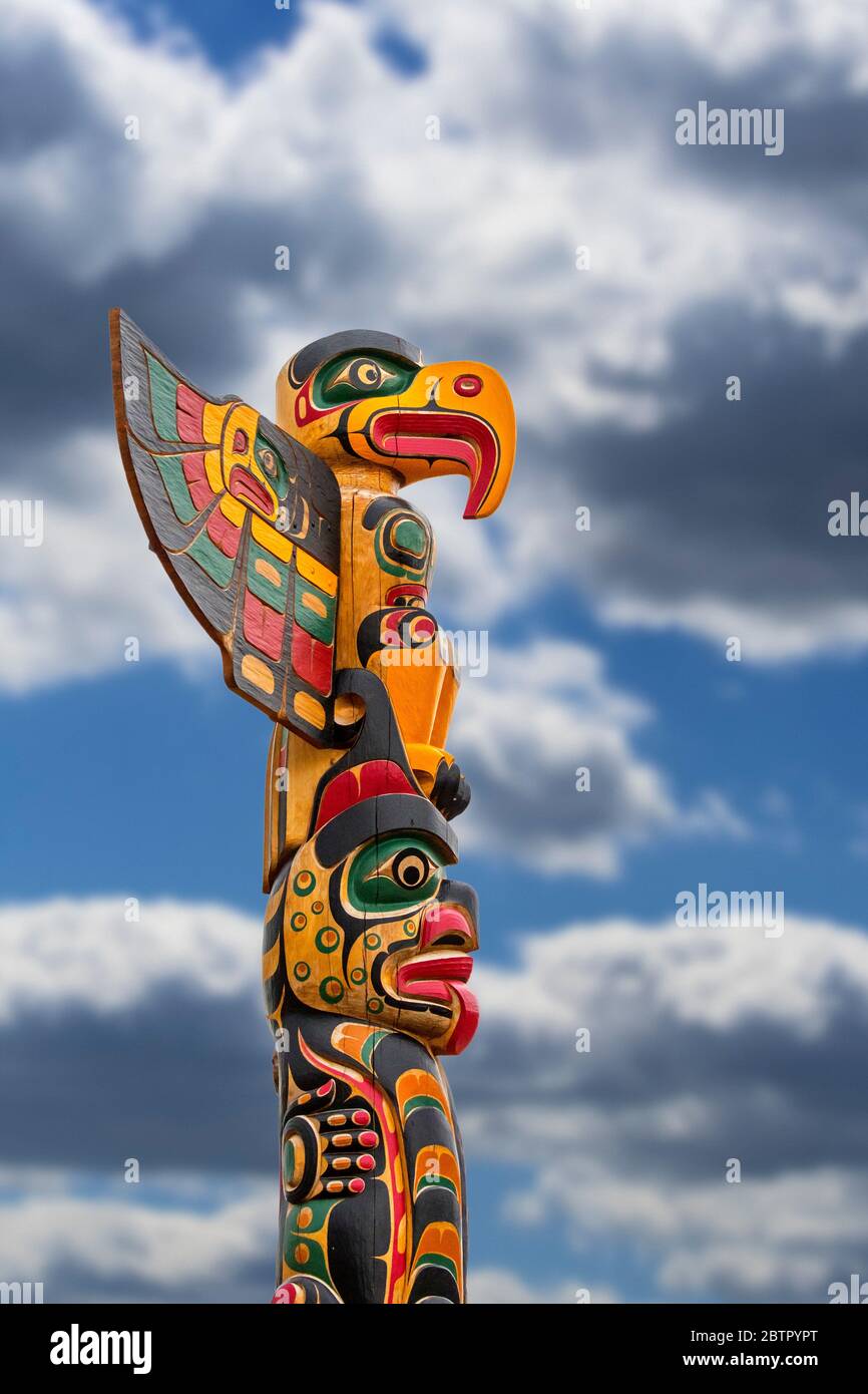 Colourful wooden carved Canadian totem pole against cloudy sky Stock Photo