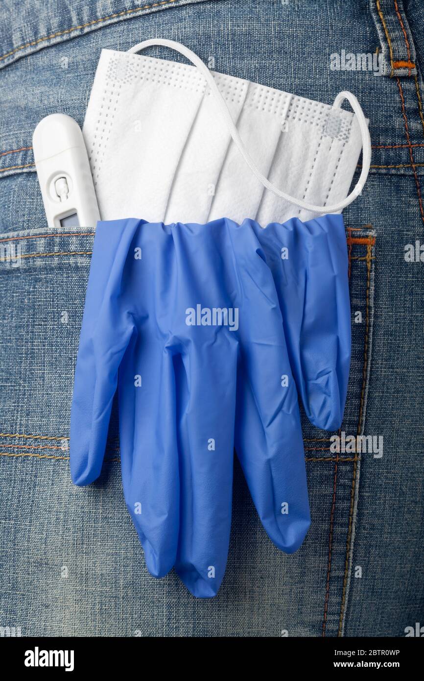 Facial mask, thermometer and latex glove in jeans back pocket Stock Photo