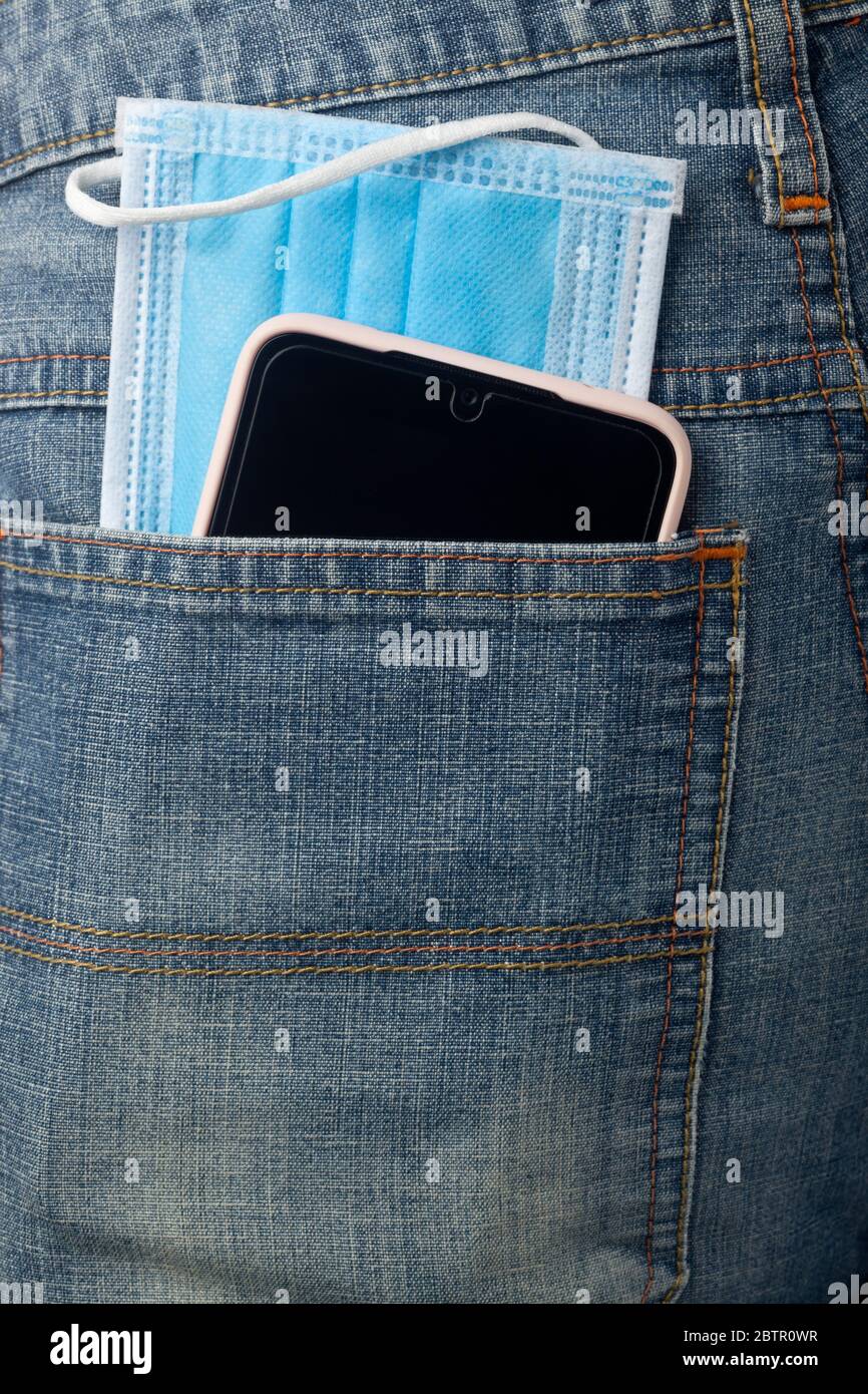 Facial mask and mobile phone in jeans back pocket Stock Photo