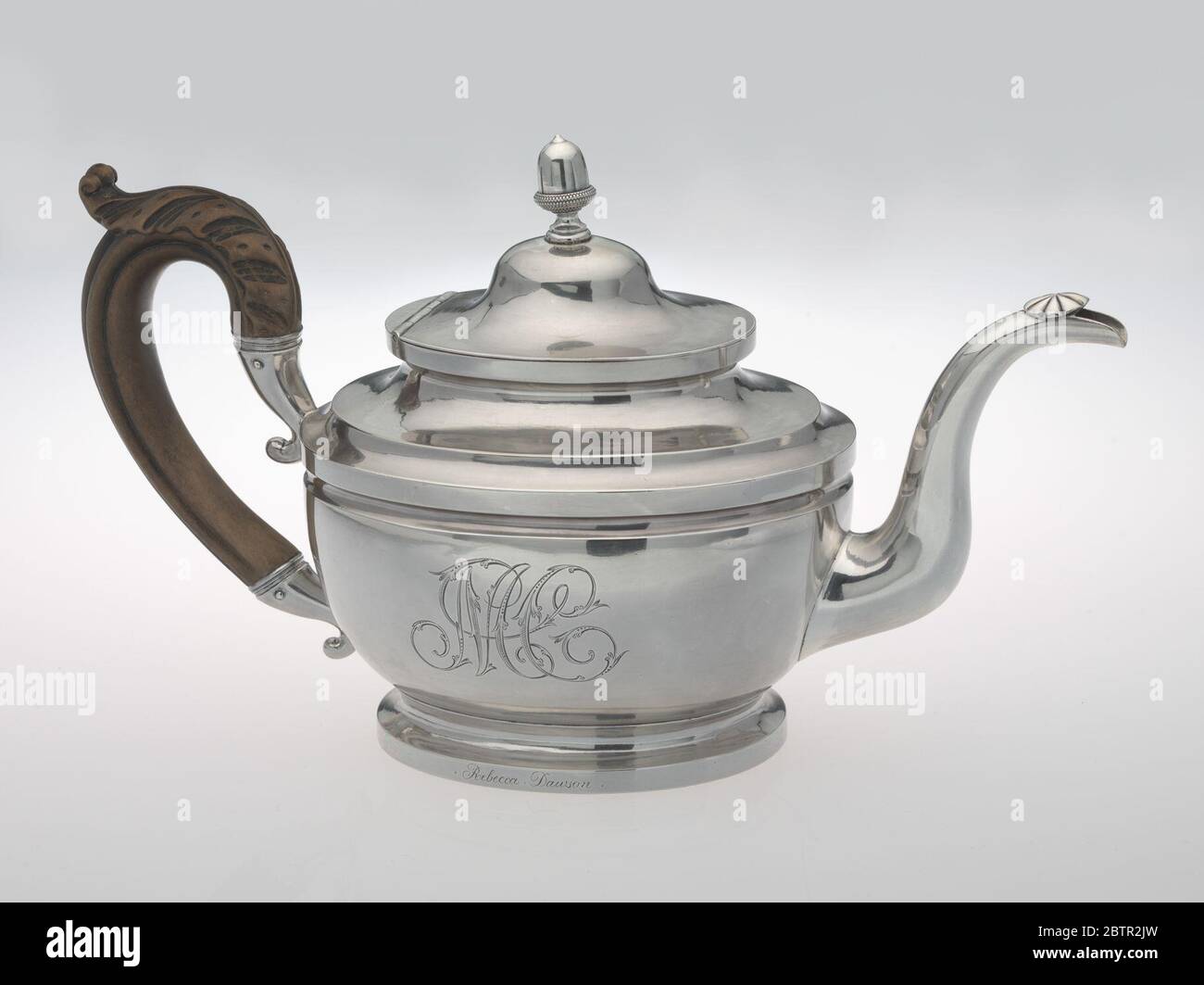 Teapot made by Peter Bentzon. The silver teapot has an oval vase-shape on a spreading pedestal foot, with curved spout capped by an incised patera and wooden leaf-capped scroll handle, and hinged domed cover with acorn finial. Stock Photo
