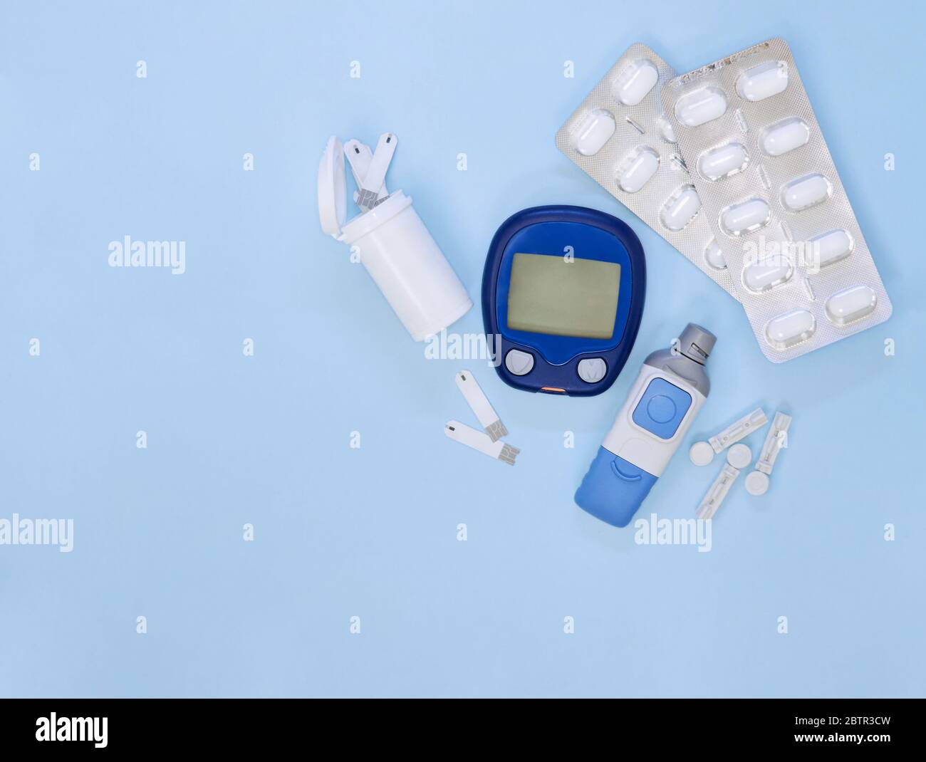Diabetic kit: glucometer, test strips, lancet, metformin tablets. Top view, blue background, empty space. Stock Photo