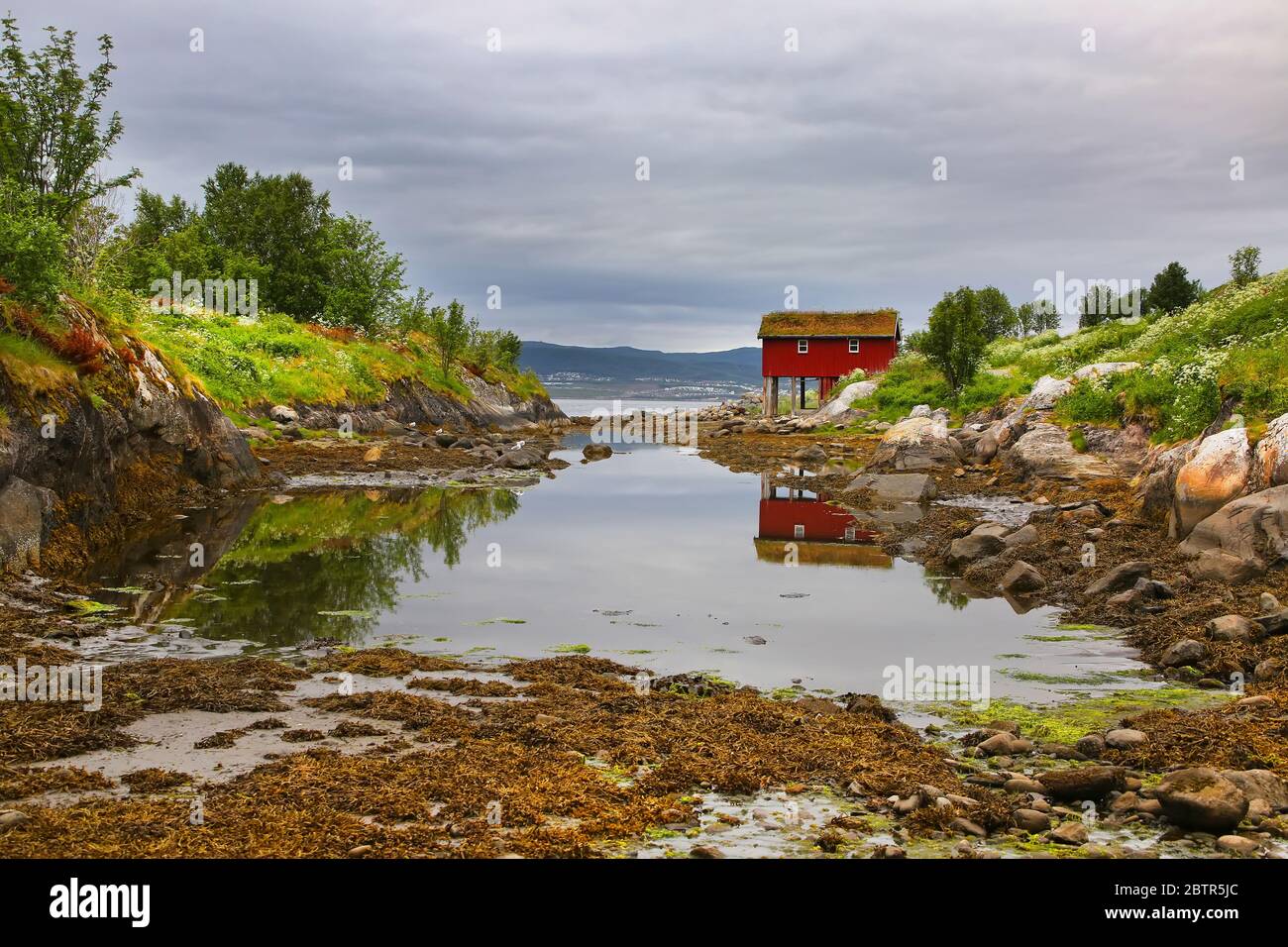 Beautiful landscape along waters edge, with a village & church & mountains in the background, Saltstraumen, Municipality of Bodo, Nordland, Norway. Stock Photo