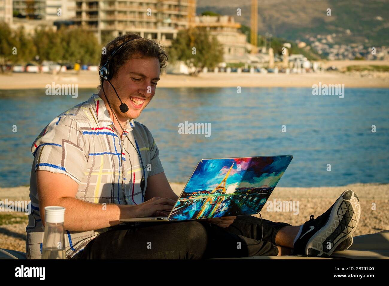 One man using laptop and headset outdoors at a beach Stock Photo