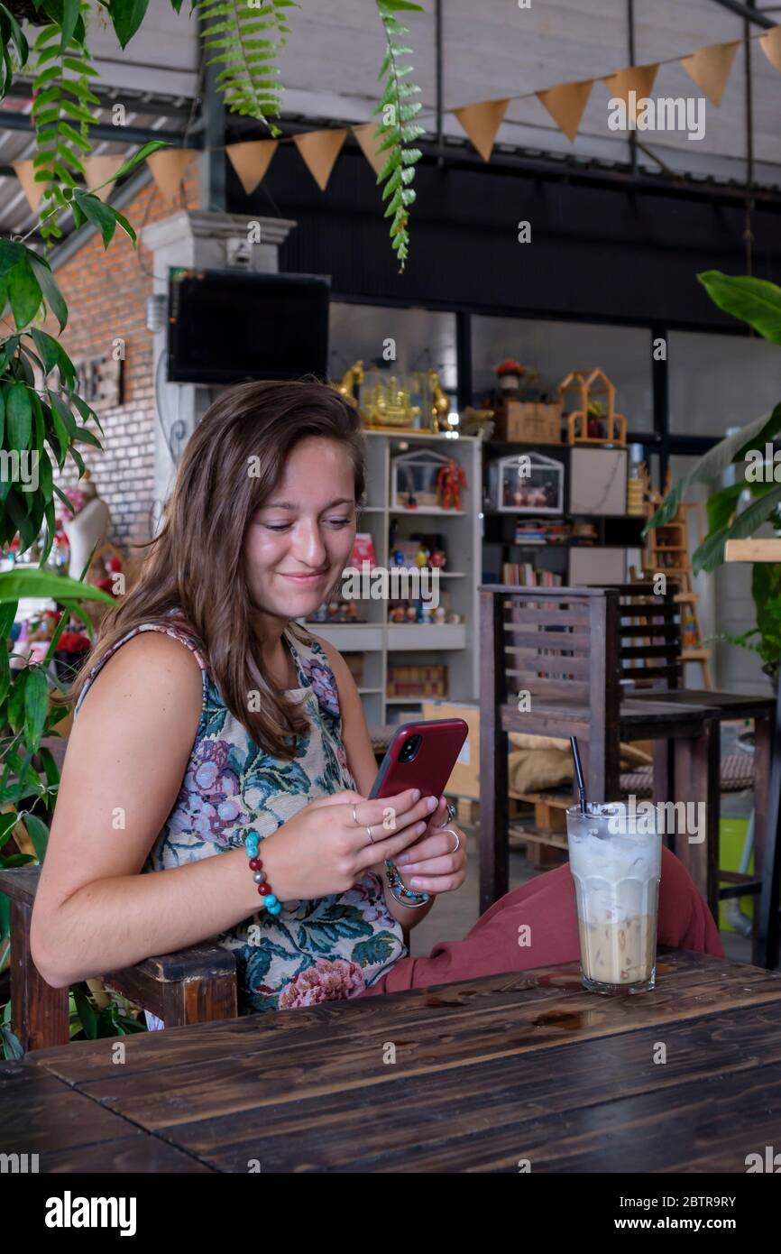 Young woman looks at her mobile phone with iced beverage on the table in a cafe Stock Photo