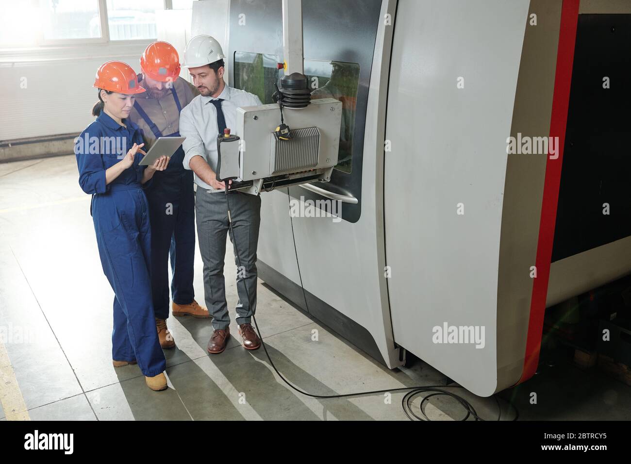 Engineers and programmer working with modern automated CNC machine in workshop Stock Photo