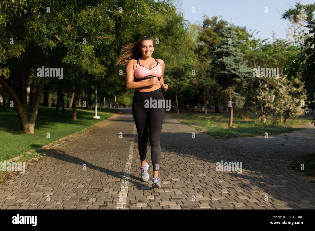 Young pretty smiling plus size woman in sporty top and leggings joyfully  running while spending time in cozy city park Stock Photo - Alamy