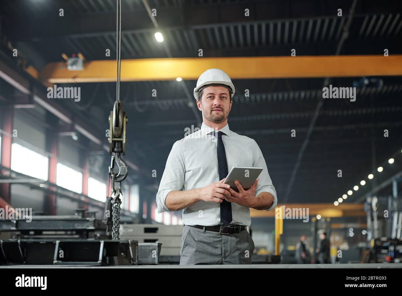 Portrait of qualified male technologist in shirt and tie standing with tablet in modern factory shop Stock Photo