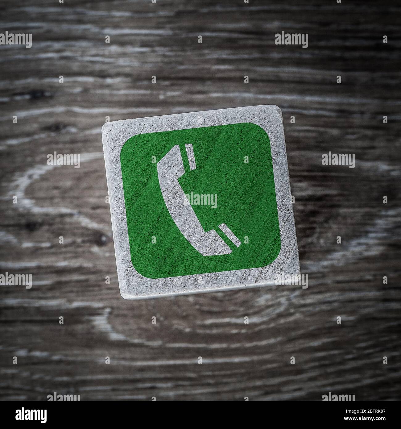 A green telephone or mobile phone sign, symbol or icon denoting connection and answering on a wooden block with a wood background and copy space Stock Photo