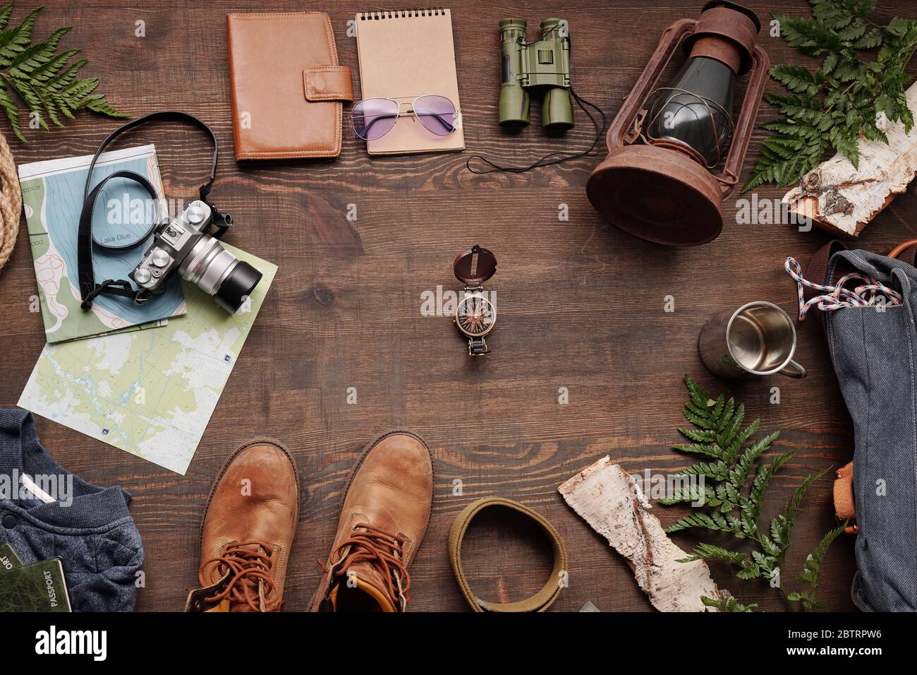Above view of navigational compass among travelers stuff such as lantern, camera, thermos mug and boots on wooden table Stock Photo