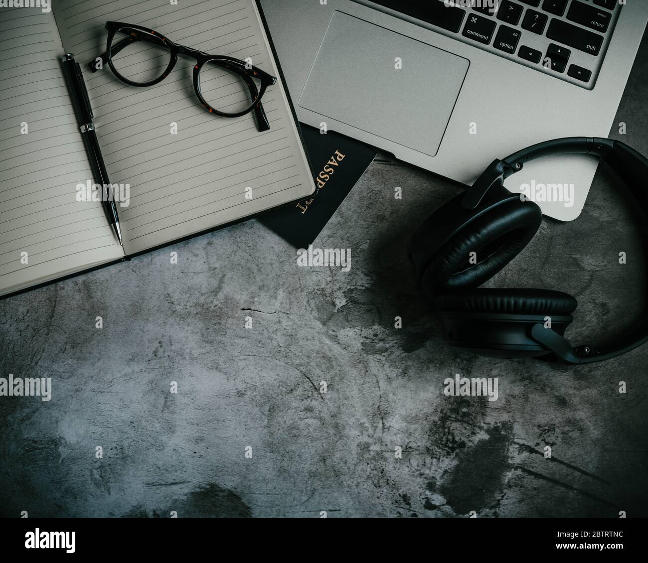 Image of an industrial flat lay design with an open notebook, glasses, passport, laptop, and black wireless headphones on a concrete background Stock Photo
