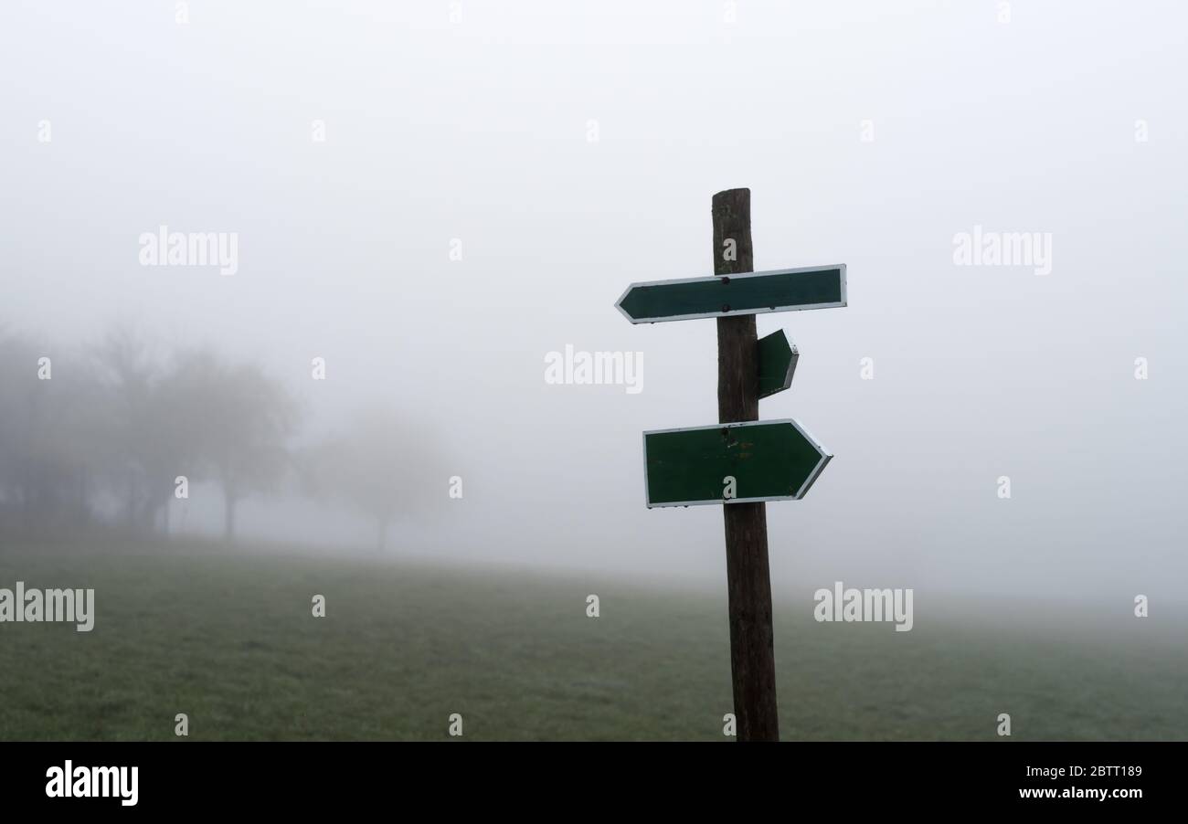 Two opposite arrows on a wooden pole with meadow and fog Stock Photo