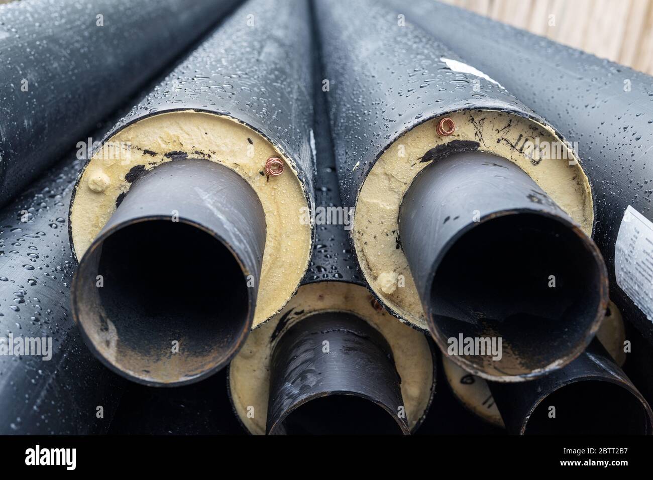 Heap of many new black insulated steel pipes at municipal construction site outdoors. Heating main district pipeline renewal or reconstruction. City Stock Photo