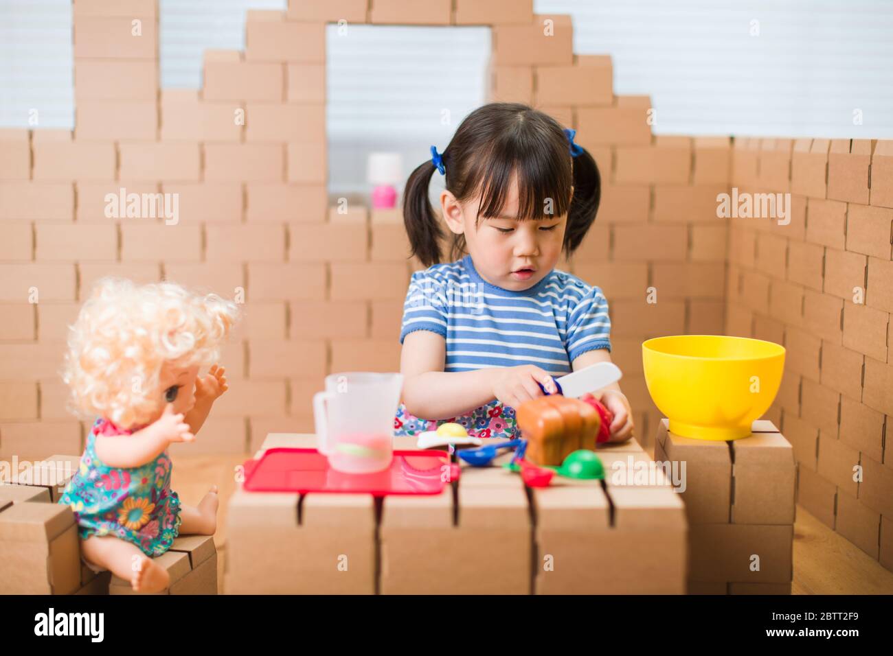 toddler girl pretend play baby care in a cardboard block house Stock