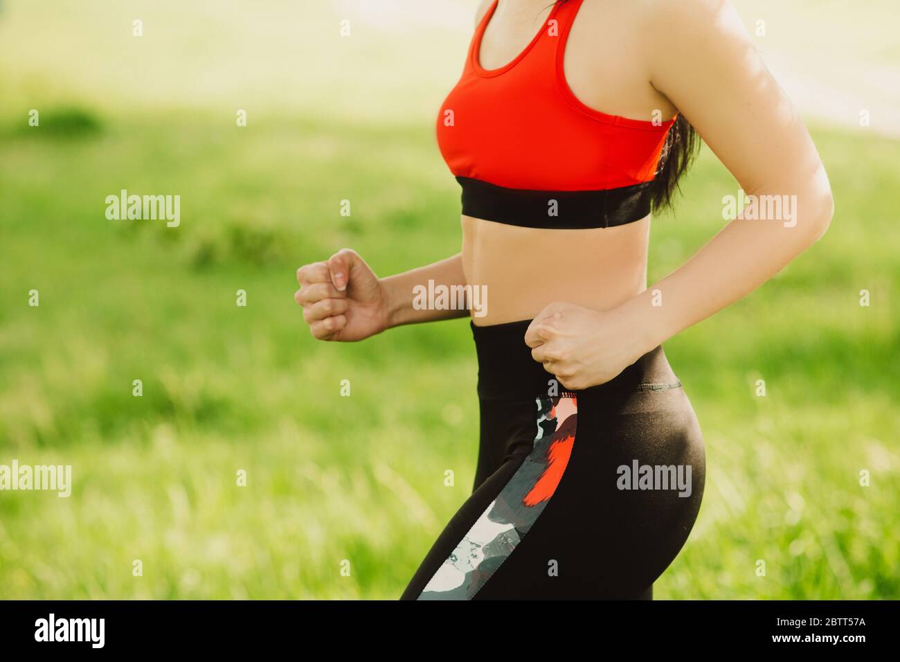The girl runs on the green grass on the sunny day. Outdoor sports. Exercises for tonus, flexibility and power. Part of the body. Stock Photo