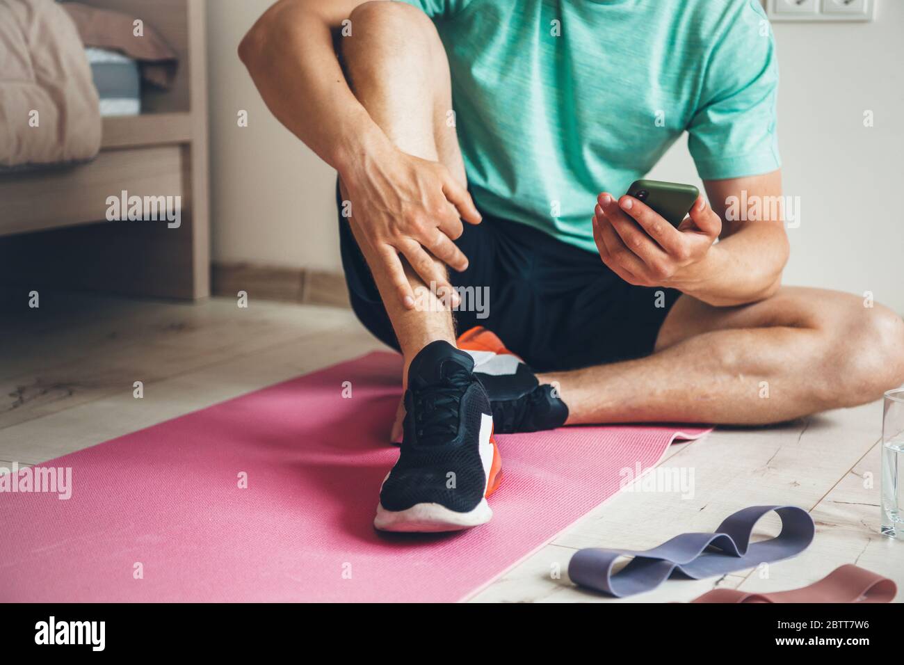 Caucasian man working out from home is resting after doing morning exercises while looking at phone Stock Photo