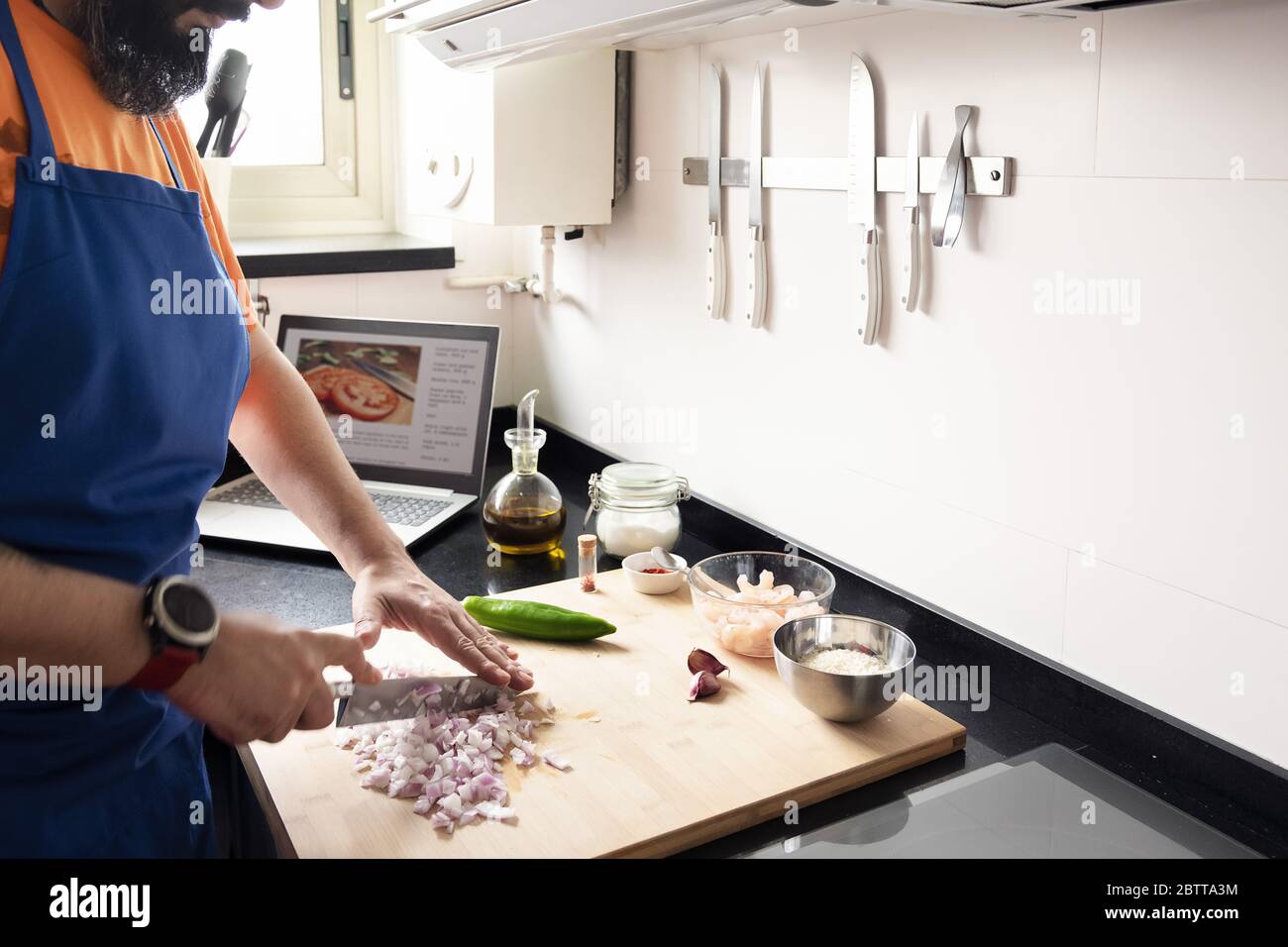 unrecognizable man chopping onions in the kitchen in the background there is a computer with the recipe he is making, concept of healthy food and lear Stock Photo