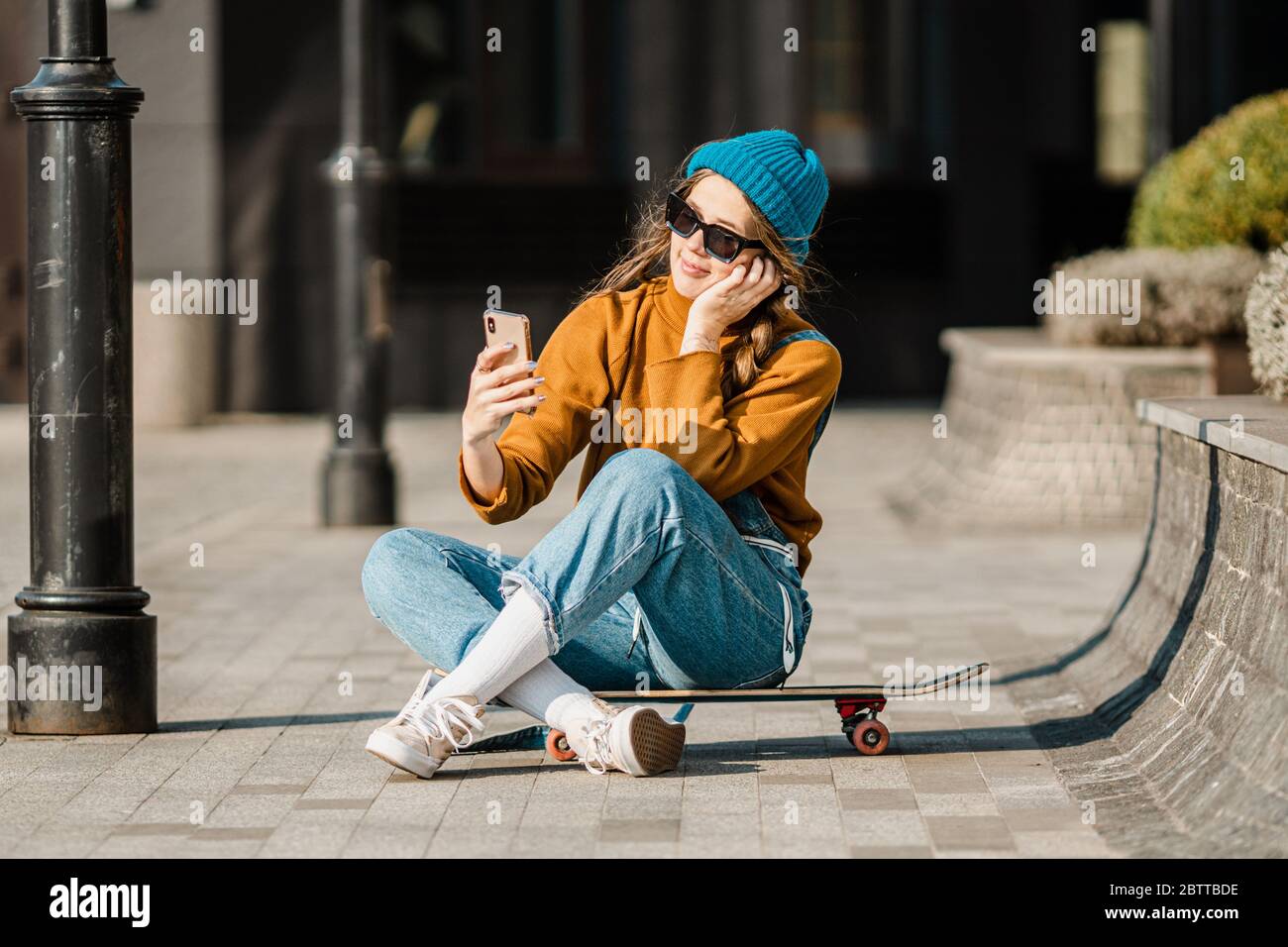 Premium Photo  Fashionable young woman hipster in fashion casual t-shirt  in trendy baseball black cap in stylish sunglasses sit on asphalt at  sunset. pretty urban cool girl in youth wear relaxes