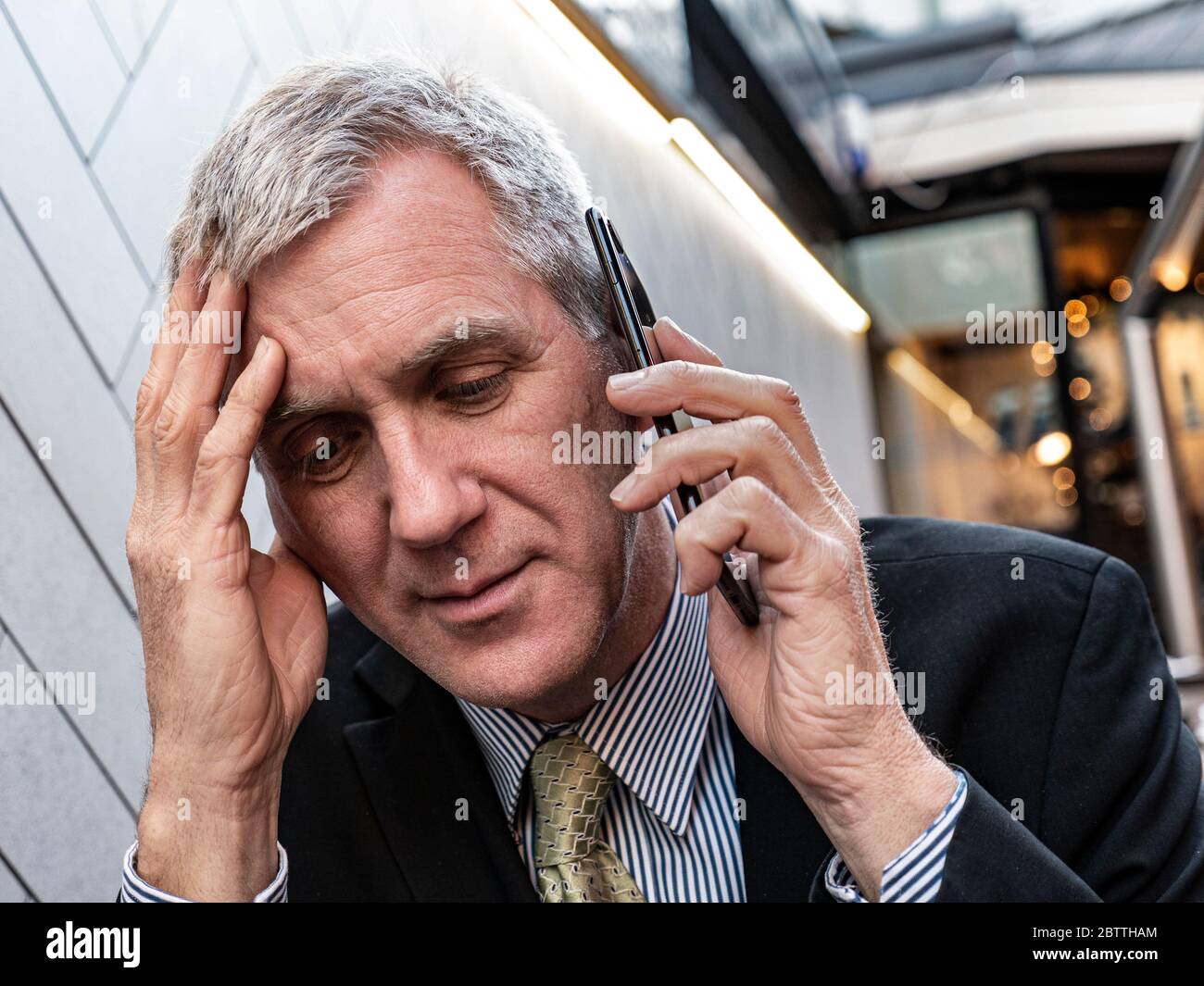 Businessman at bar table looking worried, redundant, furloughed, bad news, pensive, concerned, listening on his smartphone iPhone mobile telephone Stock Photo