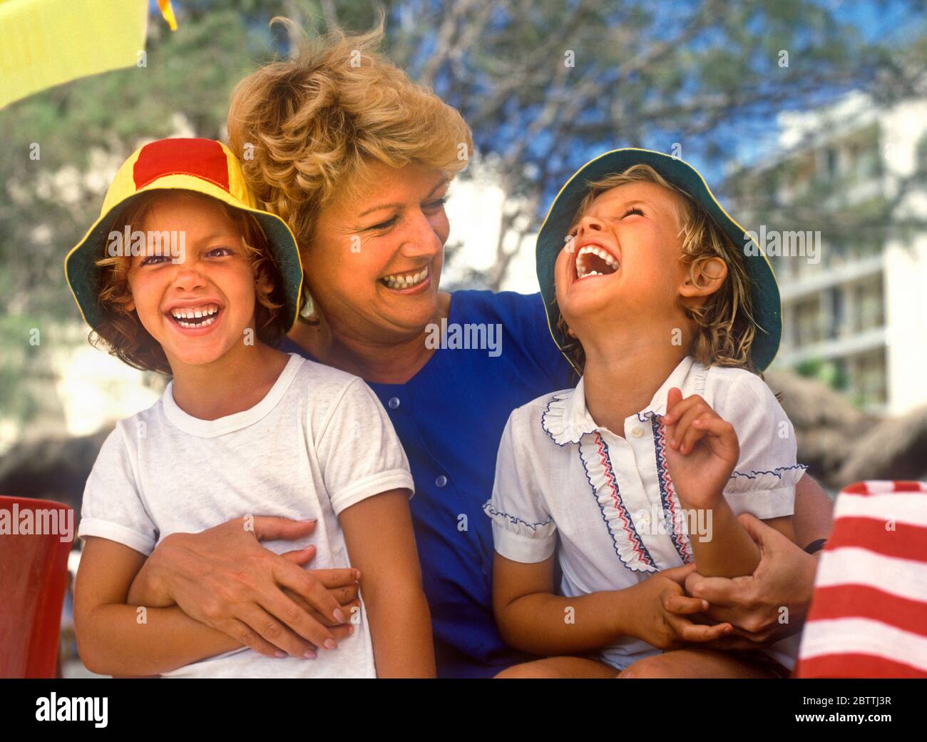 Mother and two daughters 5-7 years sitting outside and laughing together on family holiday in sunny situation Kodak moment advert Ian Shaw Kodak Photographer Stock Photo