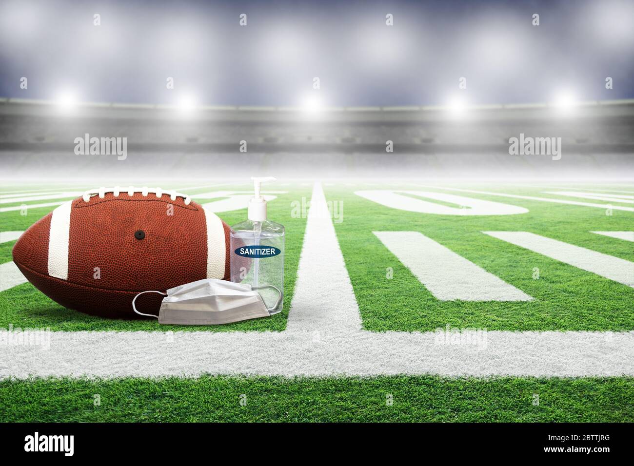 Football on field of an empty stadium with hand sanitizer and medical face mask. Concept of football played without fans as part of social distancing Stock Photo