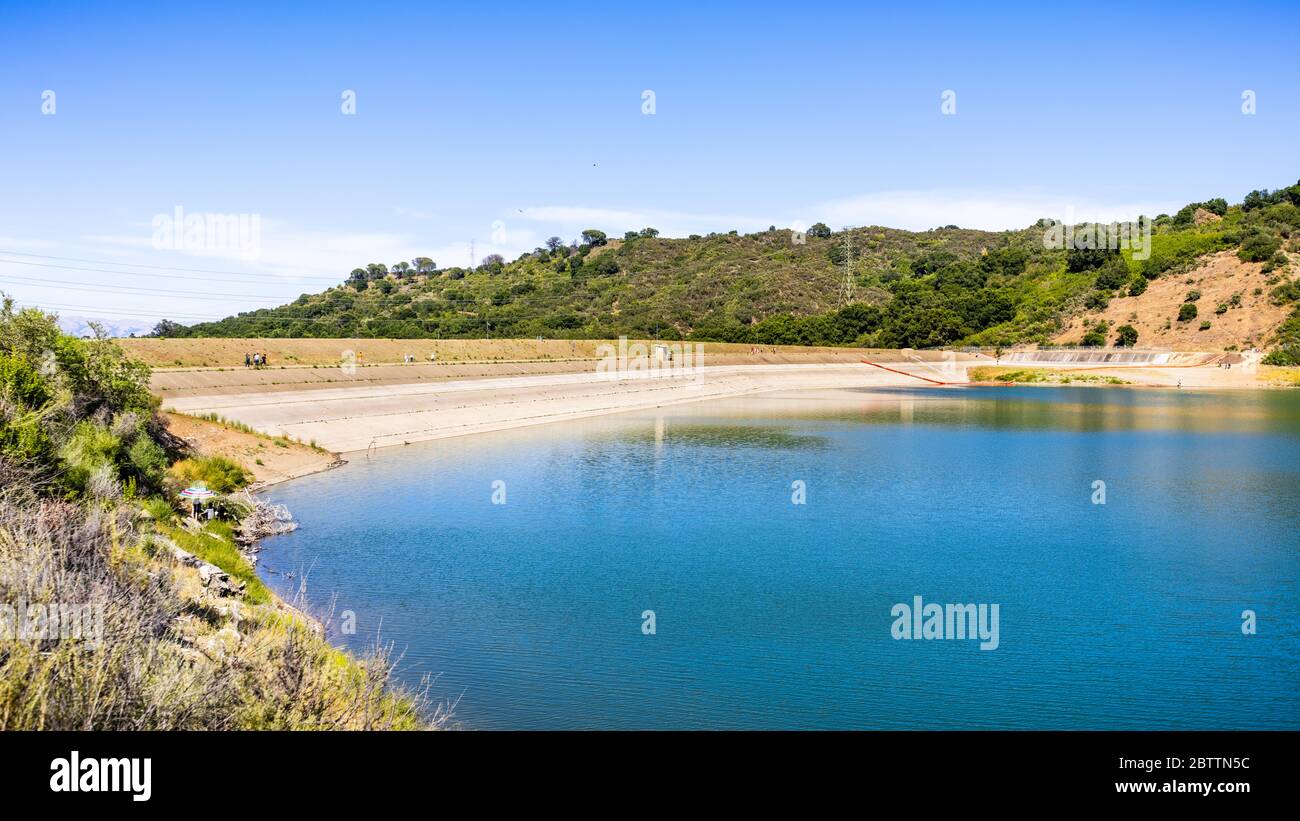 Stevens Creek reservoir on a sunny day, with people walking and relaxing on the dam and shoreline; south San Francisco bay area, California Stock Photo