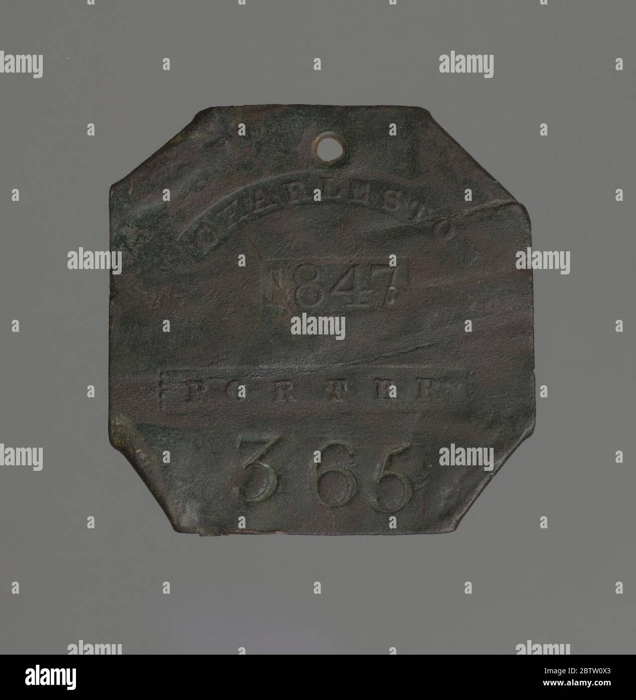 Charleston slave badge from 1847 for Porter No 365. Discolored copper square with corners folded behind and an attachment hole on the top. Die stamped: 'CHARLESTON / 1847 / PORTER / 365.' Stock Photo