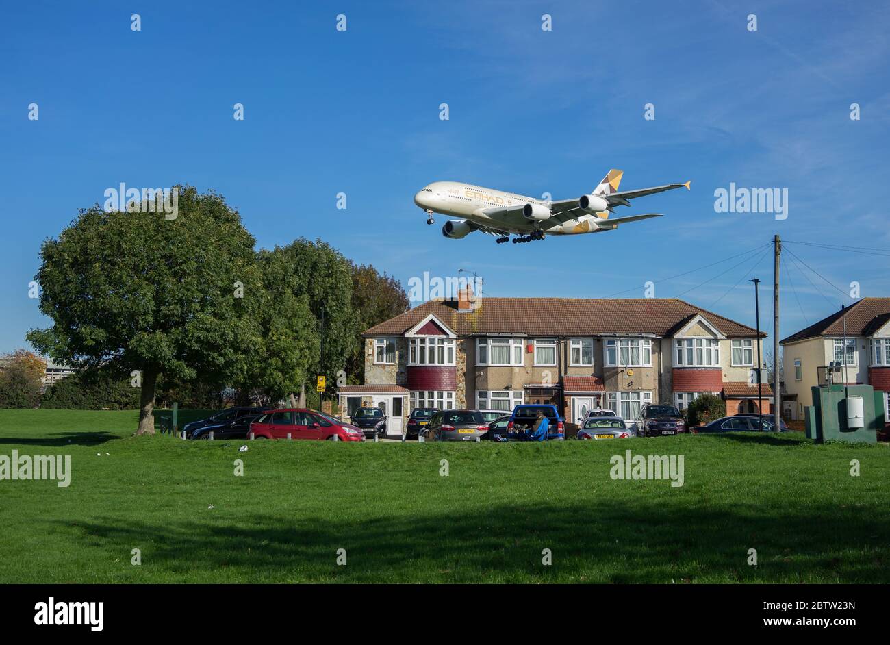 Etihad Airbus A380 landing at Heathrow Airport above residential houses on a sunny day with green grass in foreground. London Stock Photo
