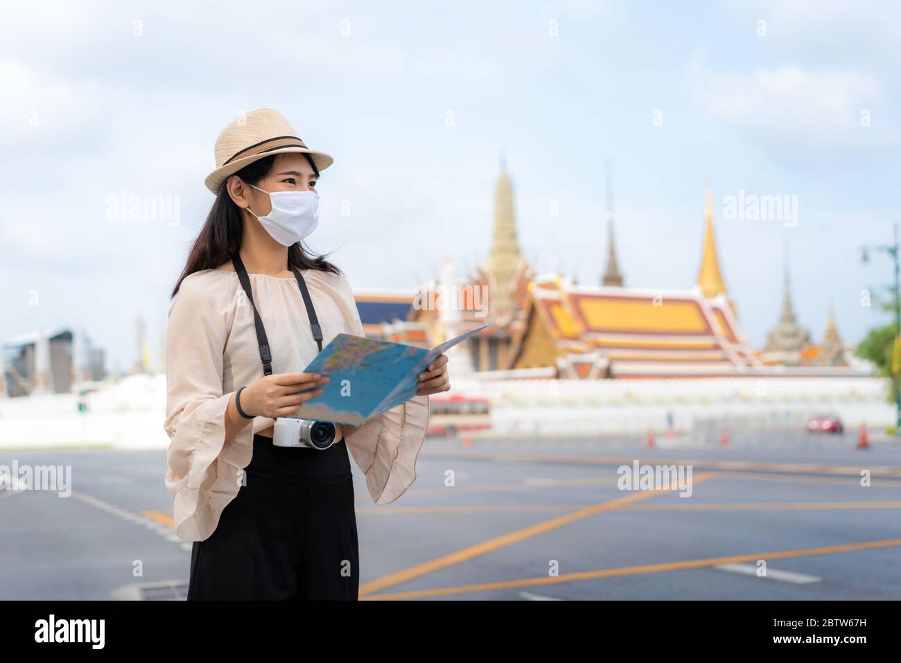 Asian woman happy tourists to travel wearing mask to protect from Covid-19 on her holidays and she looking at travel map in Wat Phra Kaew Temple in Ba Stock Photo