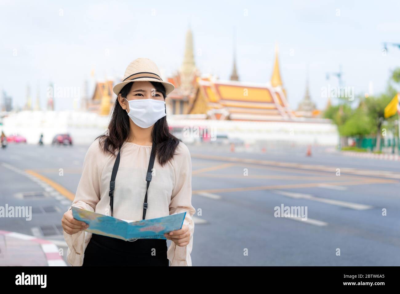 Asian woman happy tourists to travel wearing mask to protect from Covid-19 on her holidays and she looking at travel map in Wat Phra Kaew Temple in Ba Stock Photo