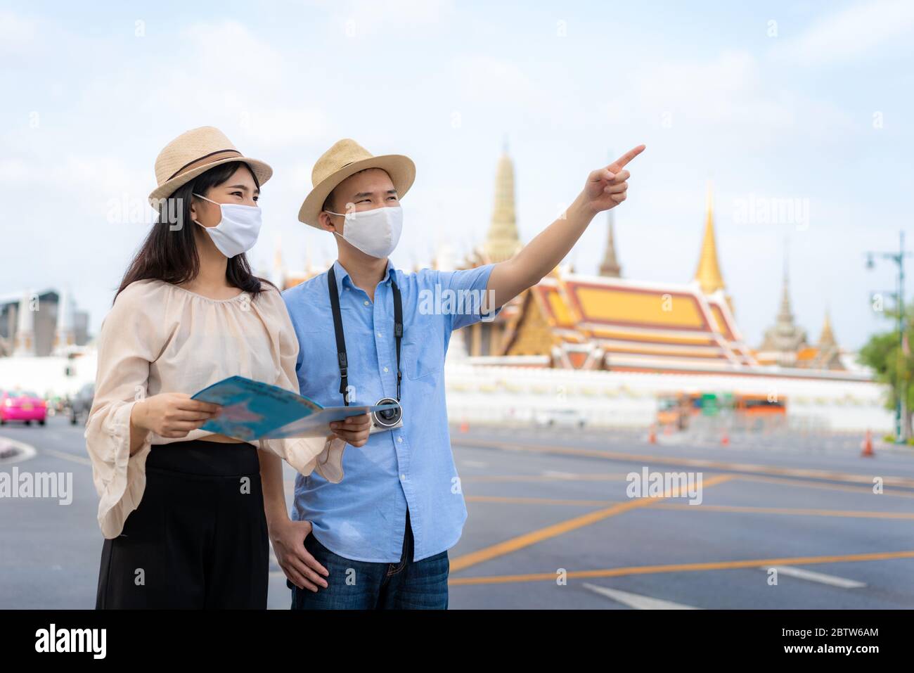 Asian couple happy tourists to travel wearing mask to protect from Covid-19 on they holidays and holding travel map and pointing in Wat Phra Kaew Temp Stock Photo