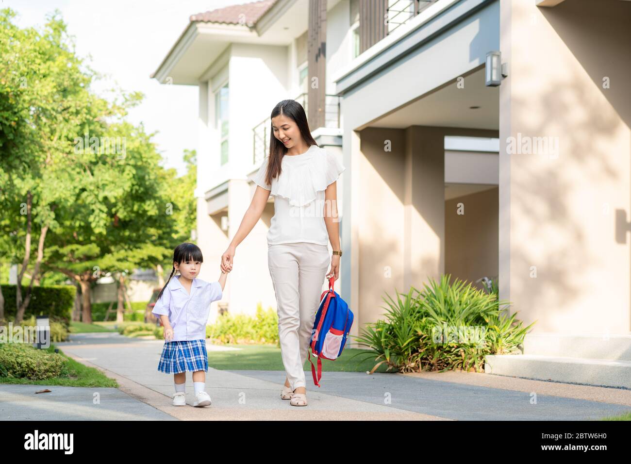 Happy Asian mother and daughter kindergarten student walking to school. Beginning of lessons. First day of fall. Parenthood or love and bonding expres Stock Photo