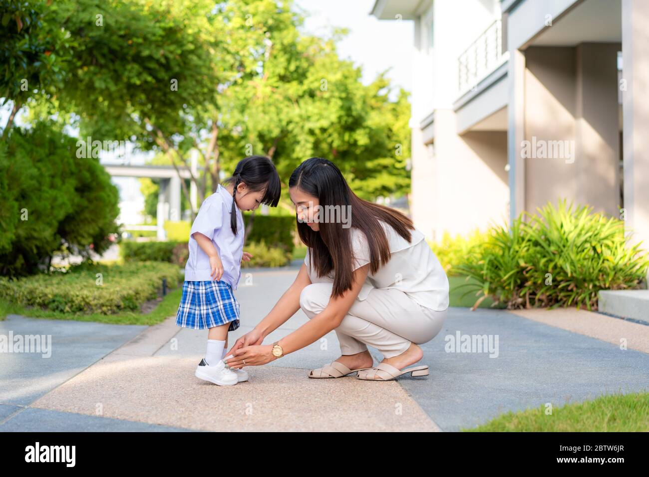 Asian mother helping her daughter put shoes on or take off at outdoor park getting ready to go out together or coming back home from school in happy f Stock Photo