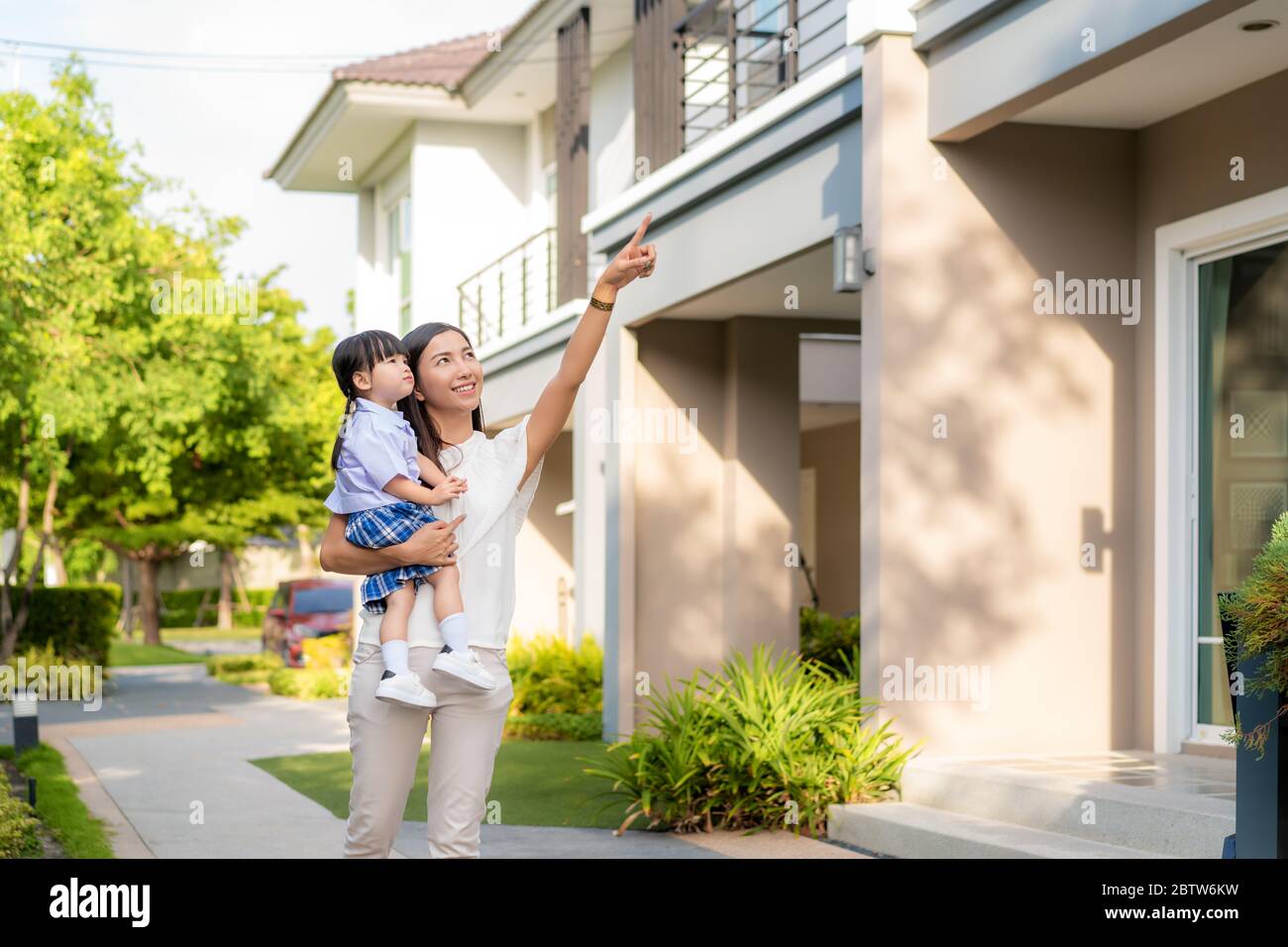 Asian family daughter and mother walking and point to their house in village. She looking happy when back to home from school. Family life love relati Stock Photo