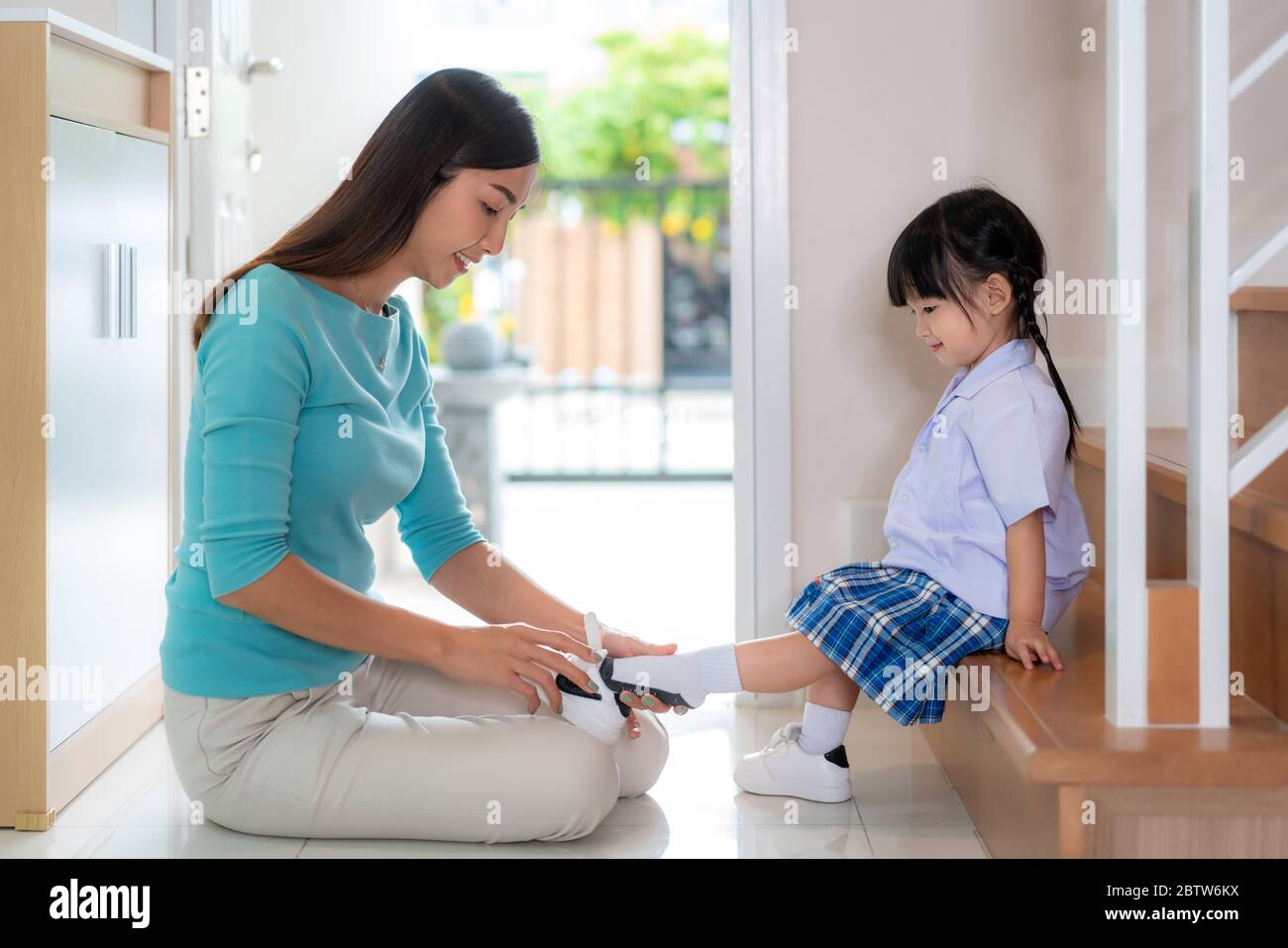 Asian mother helping her daughter put shoes on or take off at home getting ready to go out together or coming back home from school in happy family wi Stock Photo