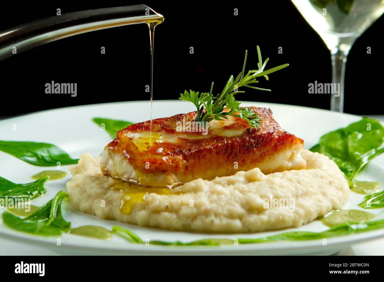 Grilled fish with mashed potatoes and spinach in anchovy butter sauce topping. Olive oil dripping. Tasty, healthy gourmet dish served with white wine. Stock Photo