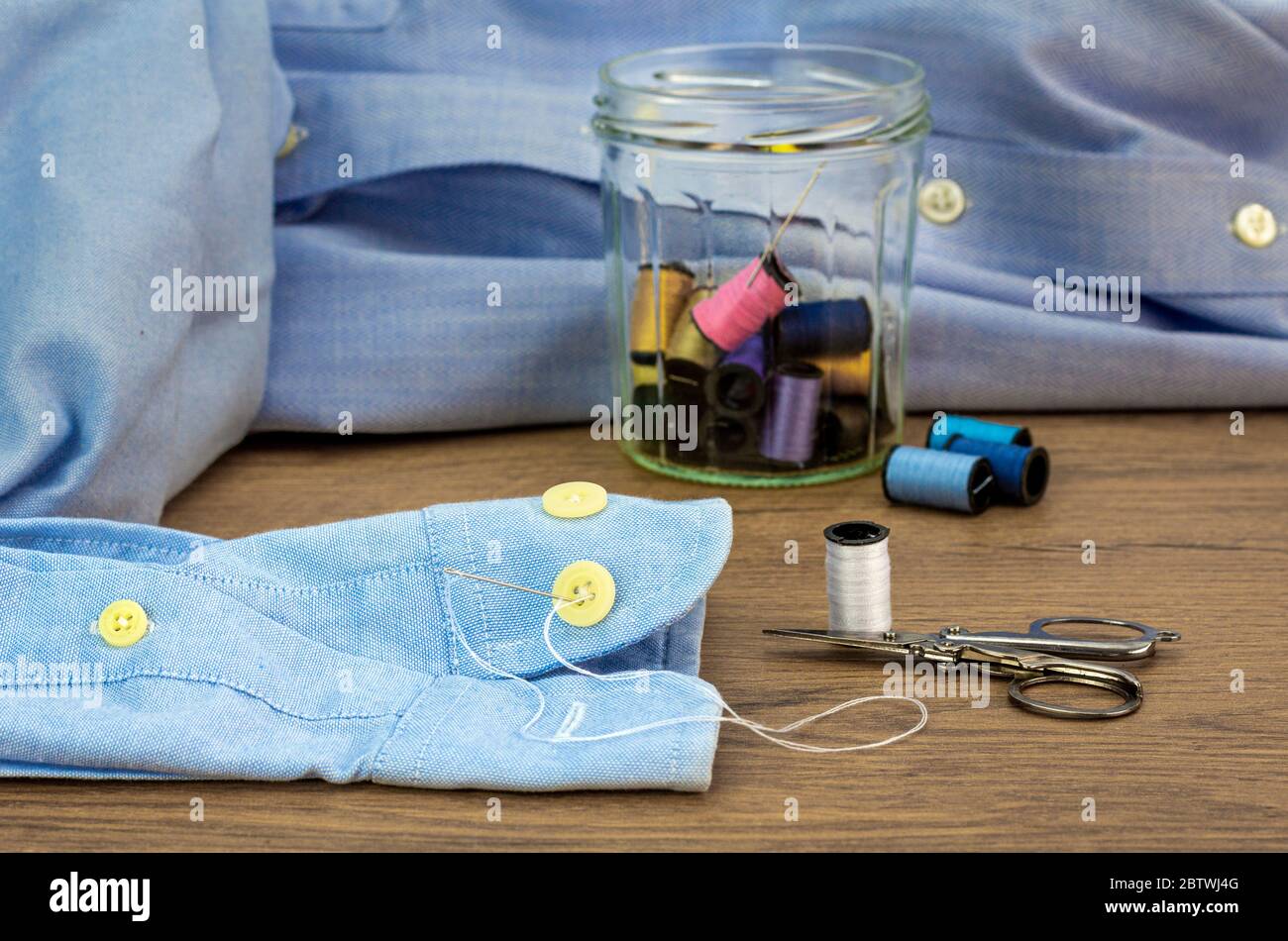 Close up of needle used to sew button on shirt, cotton reels stored in reused glass jar, repair clothing, make do and mend to reduce waste Stock Photo