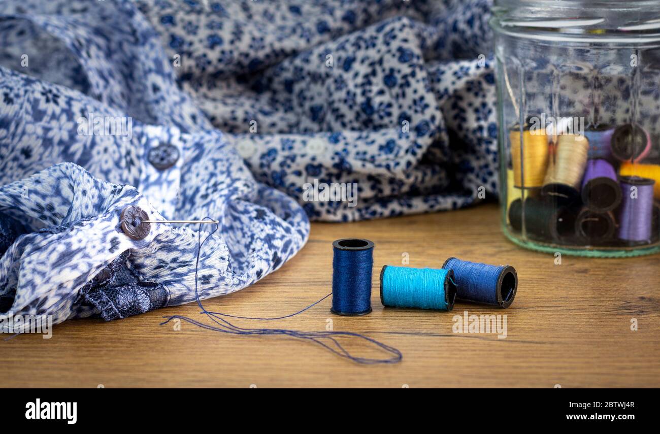 Close up of needle used to sew button on shirt, cotton reels stored in reused glass jar, repair clothing, make do and mend to reduce waste Stock Photo