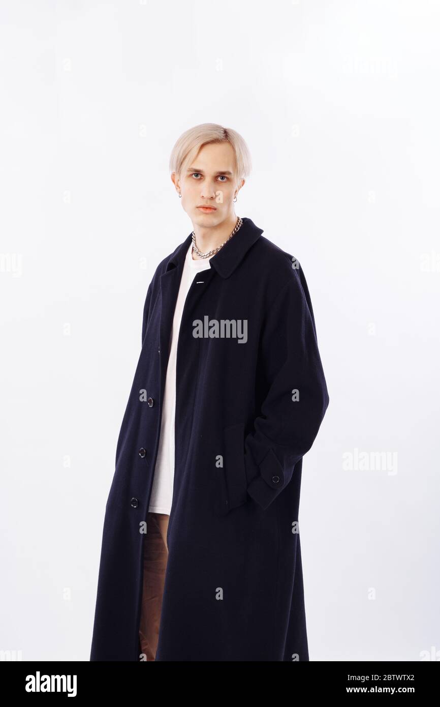 A blond man in a black coat looks into the frame. Long coat with buttons. Stock Photo