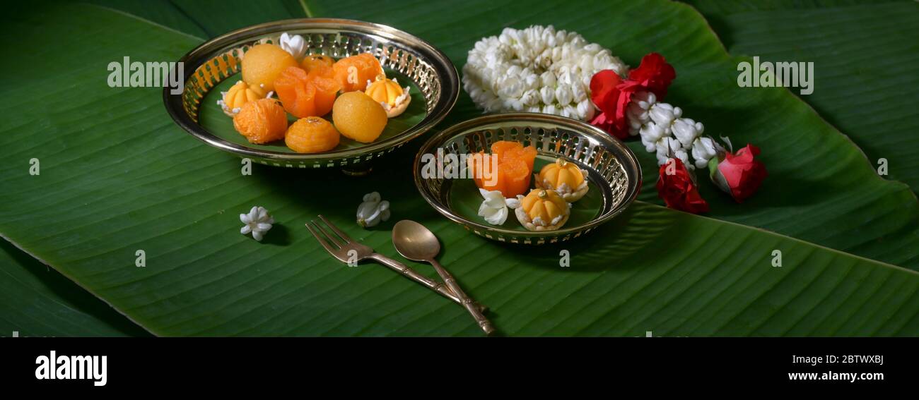 Close up view of several Thai traditional dessert serving on brass tray with brass cutlery and garland jasmine decorated on banana leaves Stock Photo