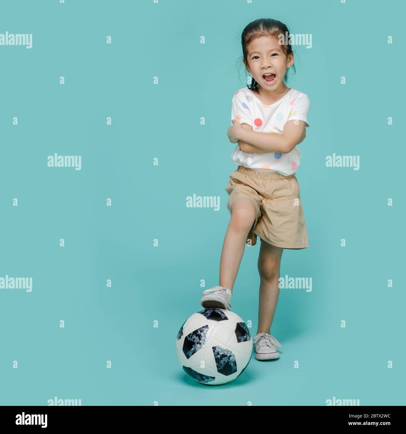 Excited Asian little girl playing football, empty space in studio shot isolated on colorful blue background Stock Photo