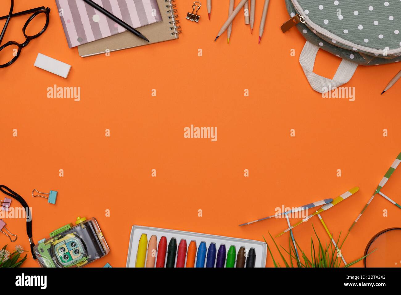 Creative flatlay of education orange table with backpack, student books, camera, colorful crayon, eye glasses, empty space isolated on orange backgrou Stock Photo