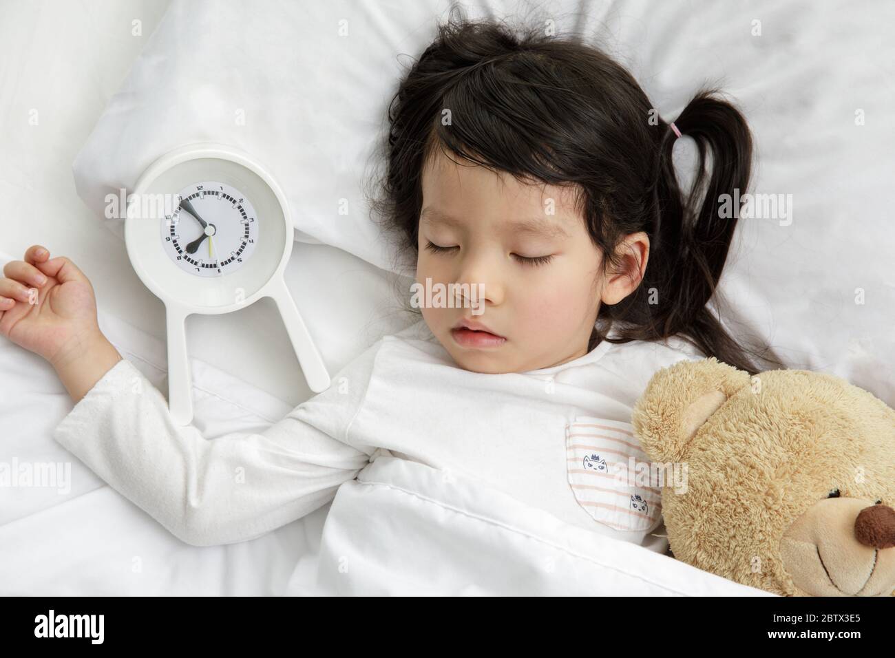 Child girl sleeping with teddy bear on the wooden bed in her bedroom