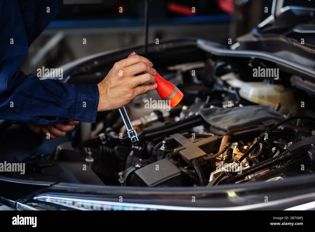 male mechanic holding and shining flashlight to checking a car engine problem Stock Photo