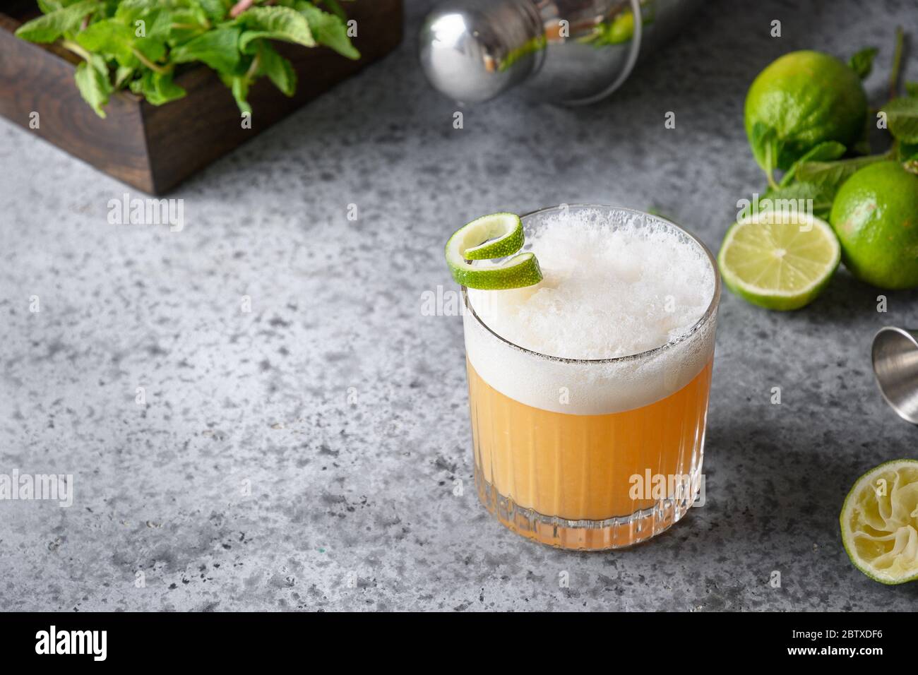 Pisco sour cocktail whiskey with lime, egg white, sugar syrup in glass on grey table. Space