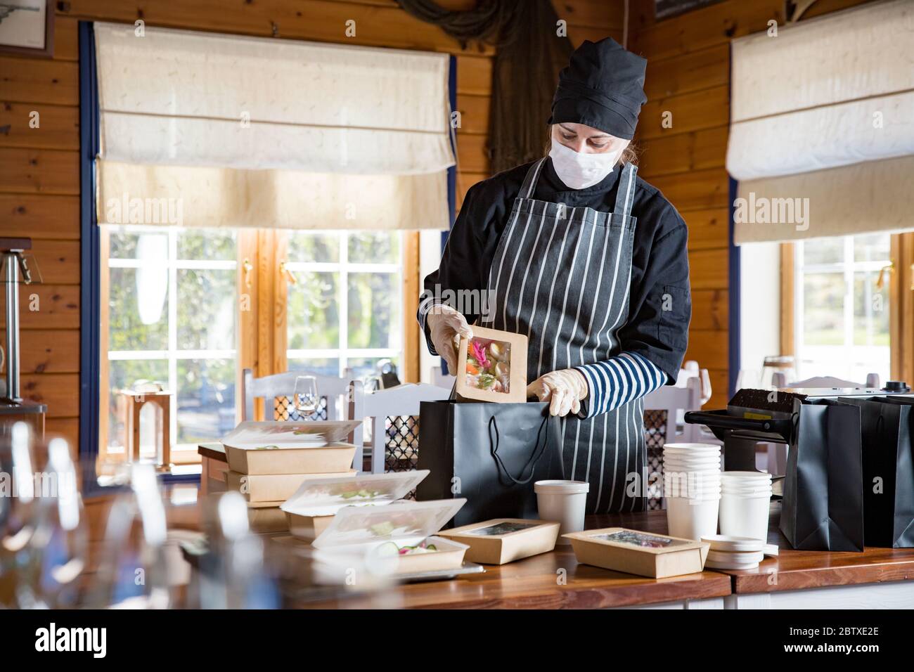 Restaurant worker wearing protective mask and gloves packing food boxed