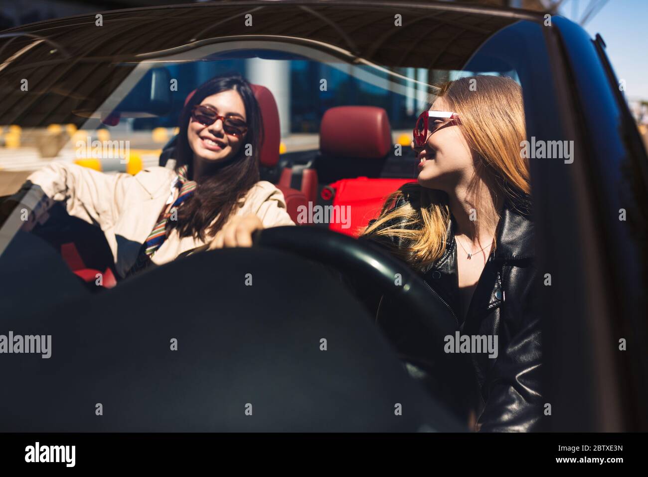 Joyful girls in sunglasses happily spending time together driving cabriolet on city streets outdoor Stock Photo