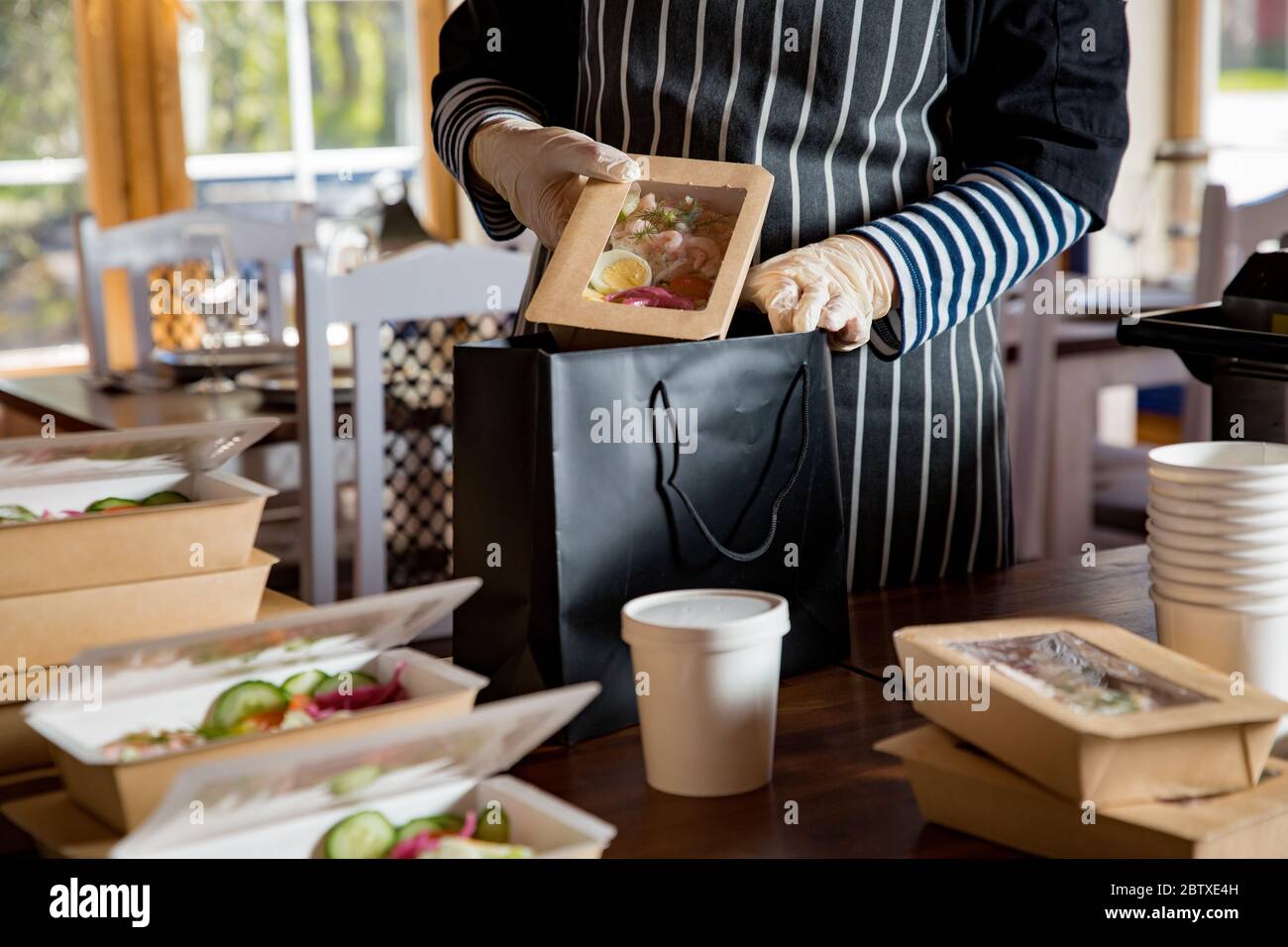 Restaurant worker wearing protective mask and gloves packing food boxed take away. Food delivery