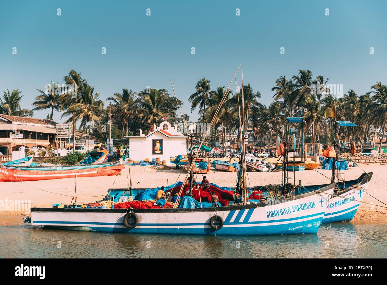 Mapusa, Anjuna, Goa, India - February 19, 2020: Fishermen Resting Near Pulled Boat From Sea Stock Photo