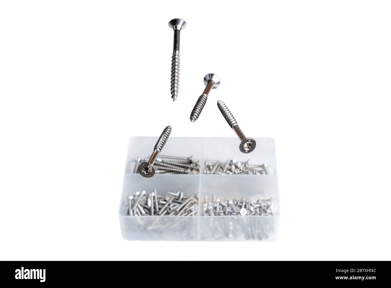 Metal screws levitating above plastic screw box isolated on white background. Manufacturing for construction industry Stock Photo