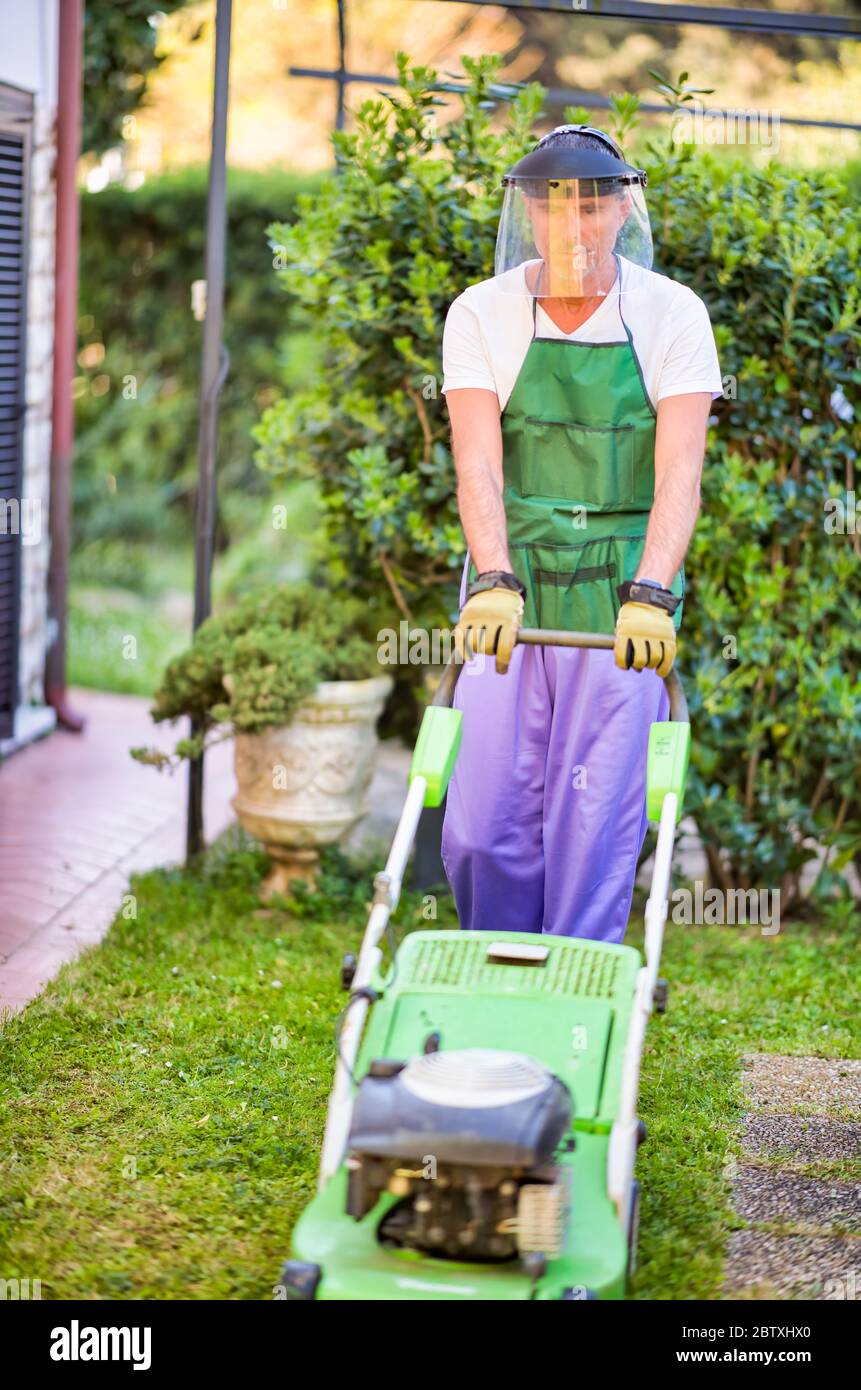 Happy male gardener wearing helmet using lawn mower Stock Photo - Alamy